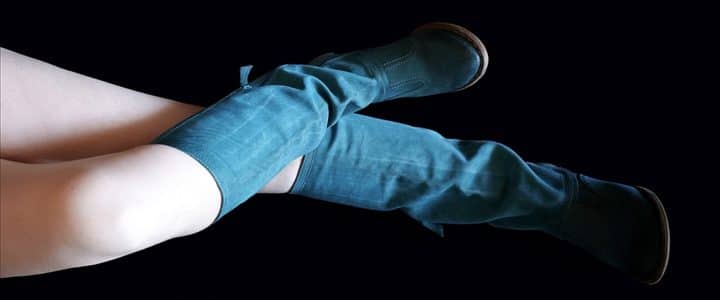 Bottes turquoise : Jambes de femme allongées sur fond noir portant des bottes au genou en suède turquoise.