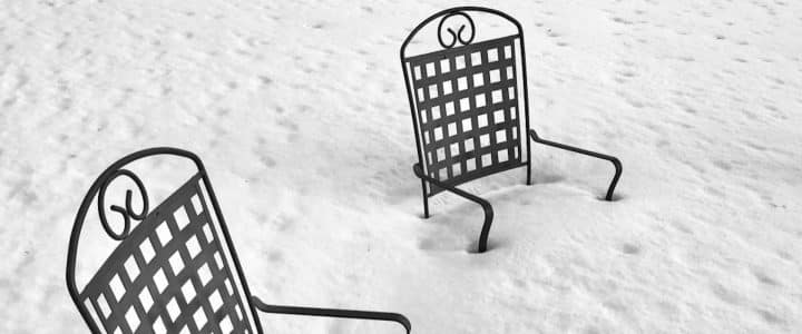 Deux chaises de jardin en métal noir ensevelies sous la neige jusqu’au siège.