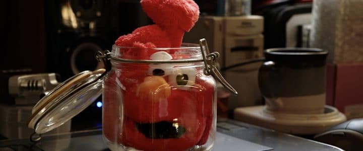 Peluche rouge Elmo coincée dans un pot de vitre placé sur un pupitre.