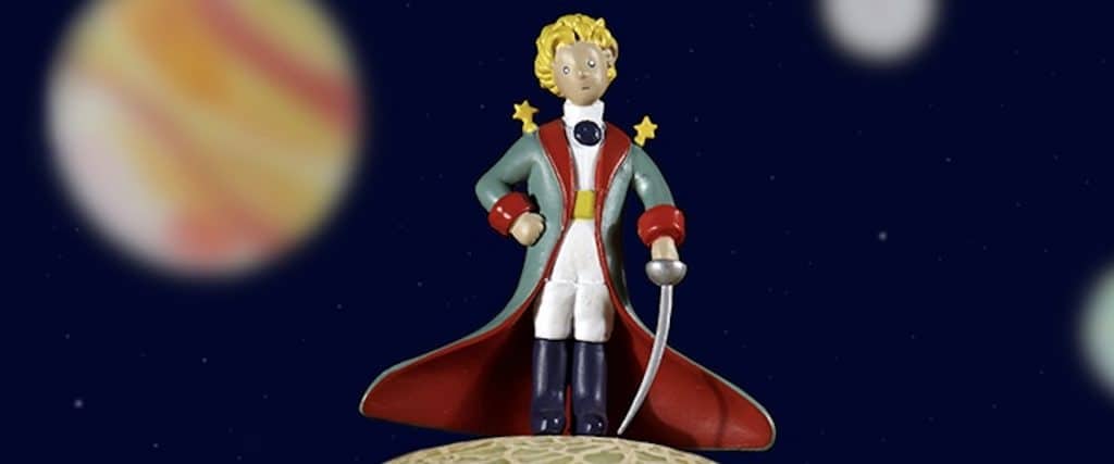 Figurine du Petit Prince sur un cantaloup avec illustrations de planètes comme fond.