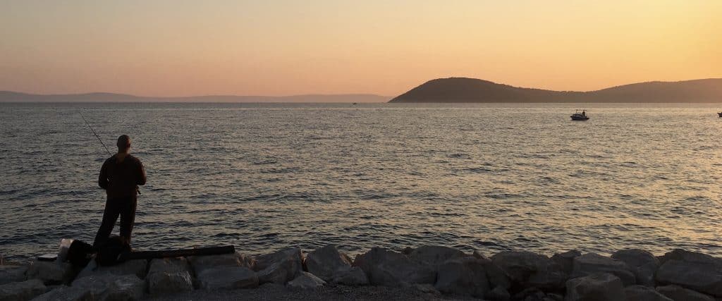 Pêcheur vu de dos devant la mer avec île lointaine au coucher de soleil à Split.
