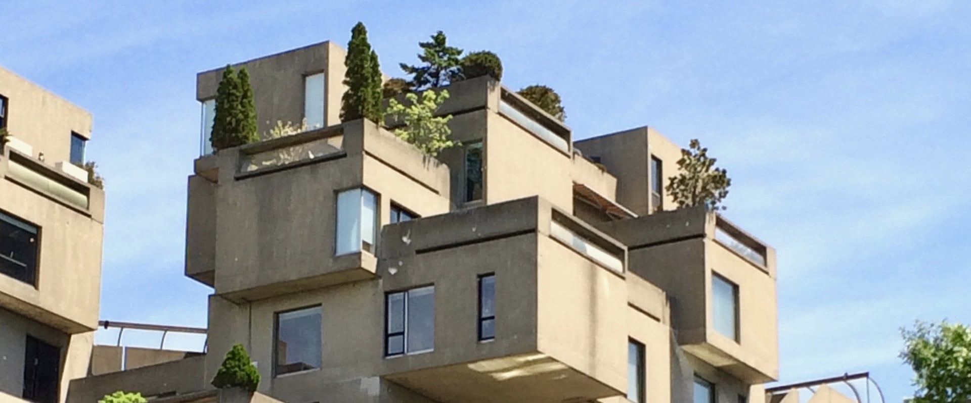 Photo de l’immeuble beige Habitat 67 sur fond de ciel bleu avec arbres verts sur les terrasses.