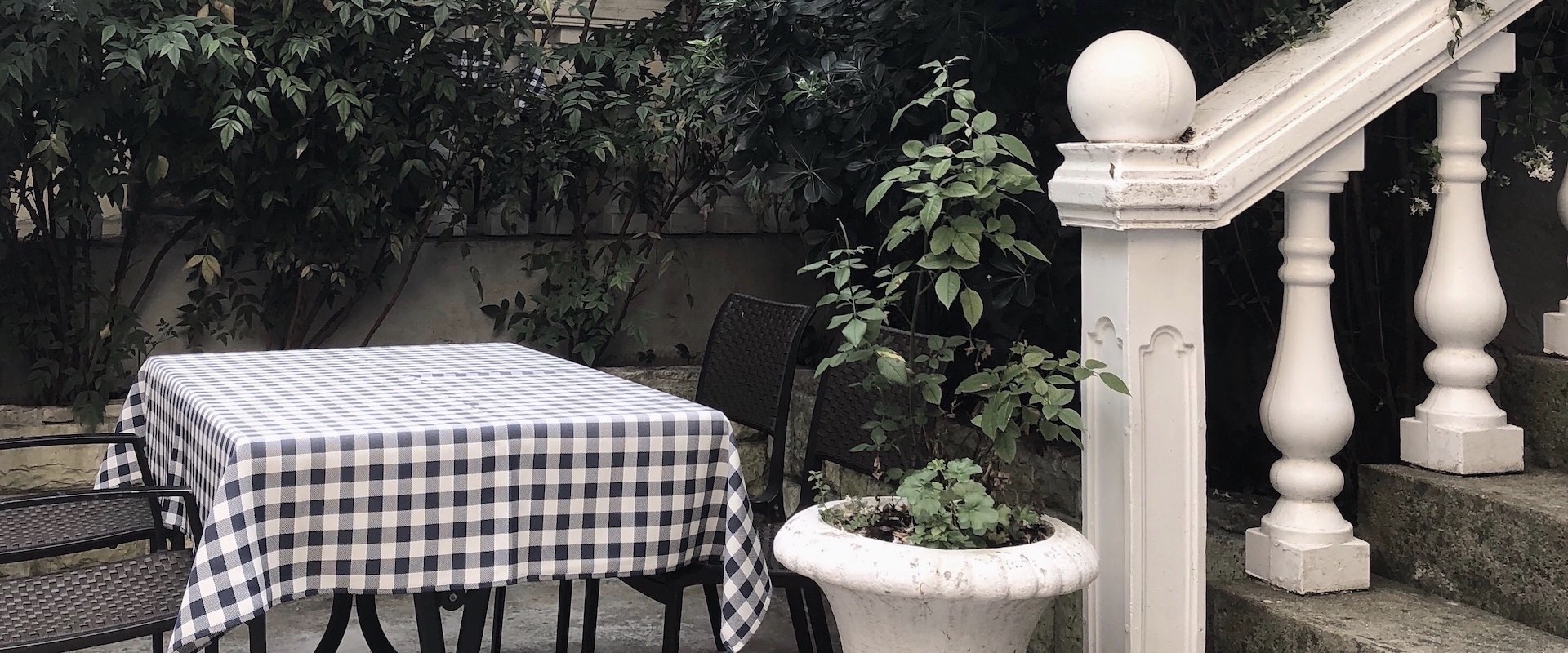 Table avec nappe à carreaux dans une cour intérieure avec un escalier en pierre et des plantes.