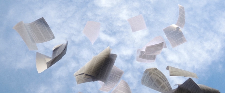 Feuilles de papier lancées en l’air contre un ciel bleu avec nuages blancs