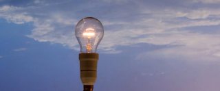 ampoule incandescente allumée devant un ciel bleu avec nuages