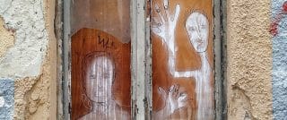 Deux personnages dessinées en graffiti sur une planche de bois dans une fenêtre d'une maison ayant besoin d'entretien.
