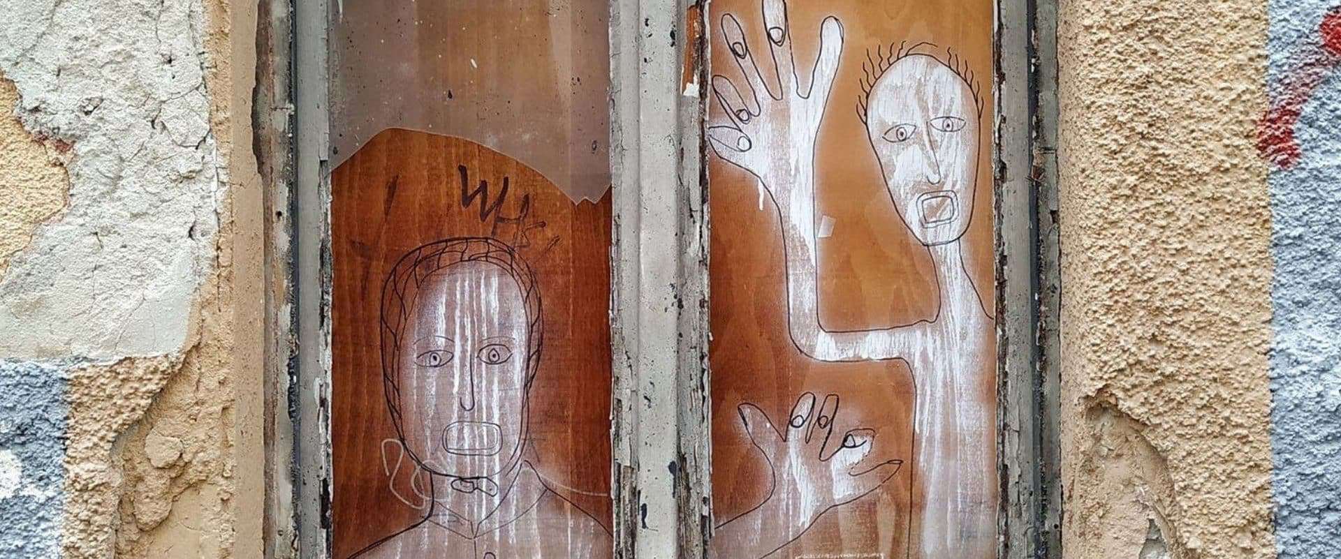 Deux personnages dessinées en graffiti sur une planche de bois dans une fenêtre d'une maison ayant besoin d'entretien.