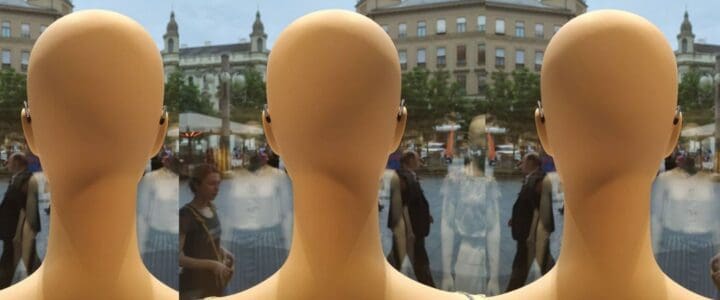 Trois têtes de mannequins dans une vitrine qui regardent les passants.