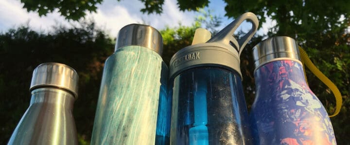 4 bouteilles d’eau en contre-plongée au soleil avec verdure en arrière-plan.