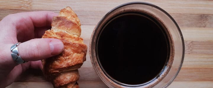 Main avec bague qui tient un petit croissant près d'une tasse de café