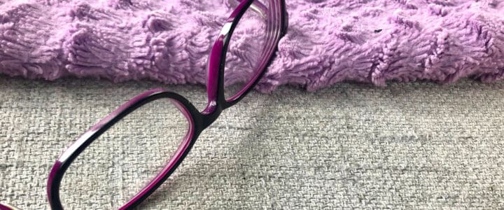 Lunettes mauves sur couverture mauve et coussin gris