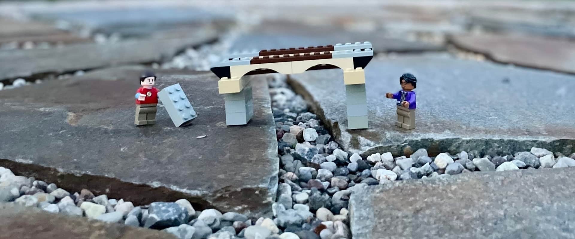 Deux bonhommes LEGO à côté d'un pont en LEGO sur des pierres à l'extérieur.