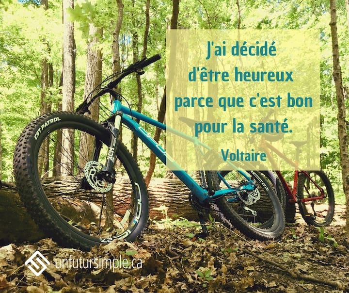 Citation de Voltaire: J’ai décidé d’être heureux parce que c’est bon pour la santé. Vélos de montagne bleu et rouge reposant sur un tronc d’arbre dans une forêt.