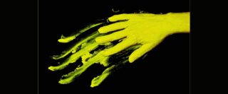 Main couverte de peinture jaune qui laisse une trace sur un fond noir