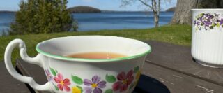 Tasse de thé sur le bras d’un fauteuil devant un lac.
